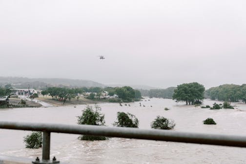 Helicopter flies over flooded area with treetops visible over water line.