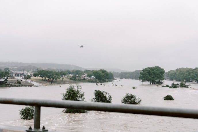 Helicopter flies over flooded area with treetops visible over water line.