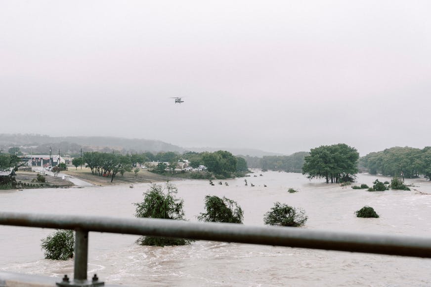 Helicopter flies over flooded area with treetops visible over water line.