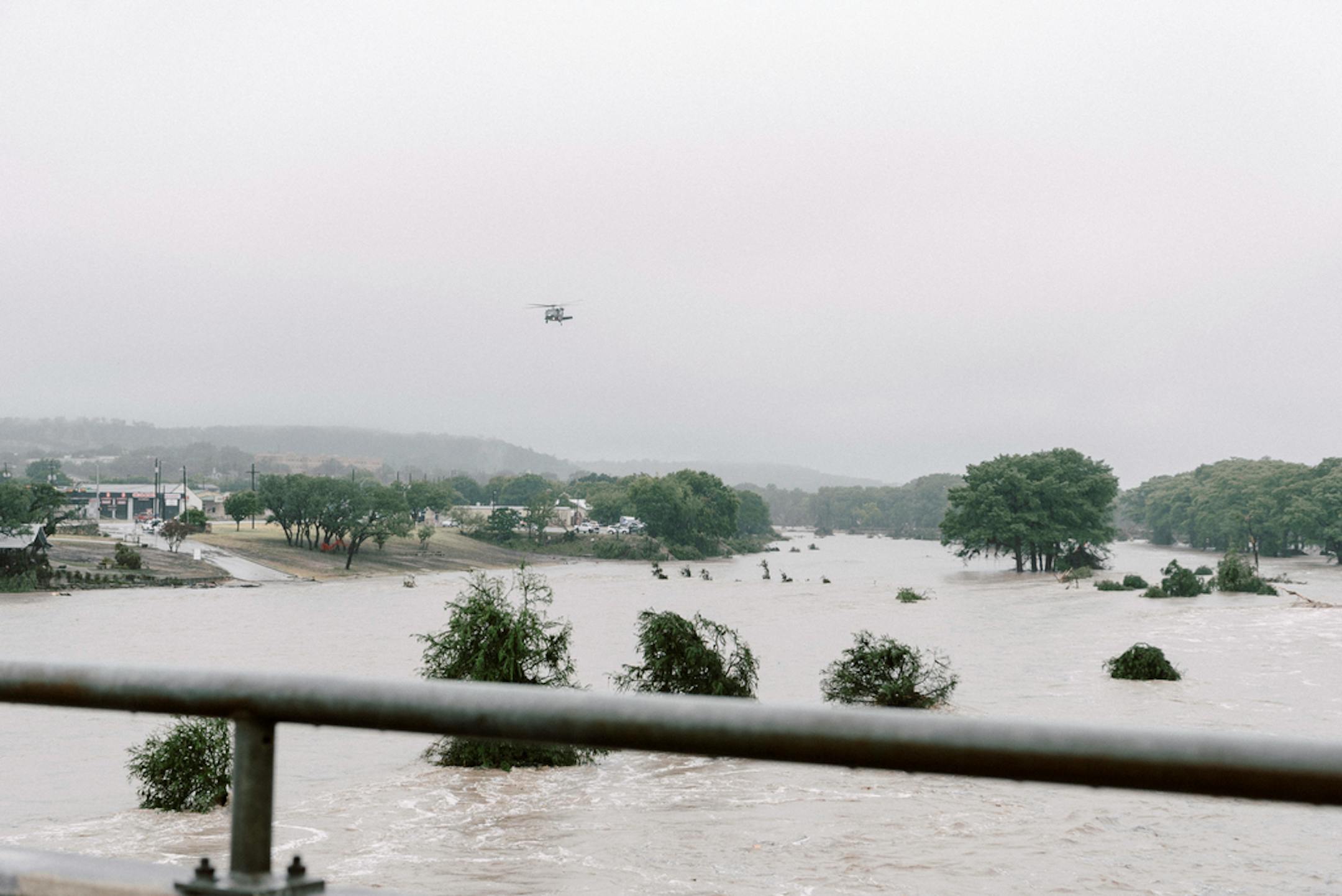 Helicopter flies over flooded area with treetops visible over water line.