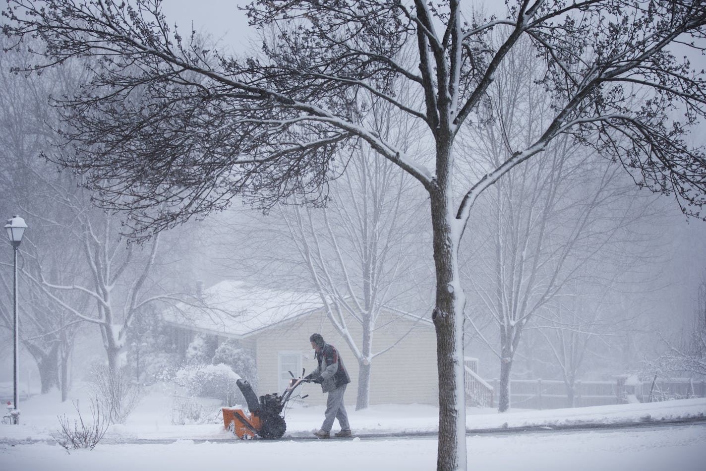 A man runs a snowblowers to clear his driveway during an early spring snowstorm in Lakeville.