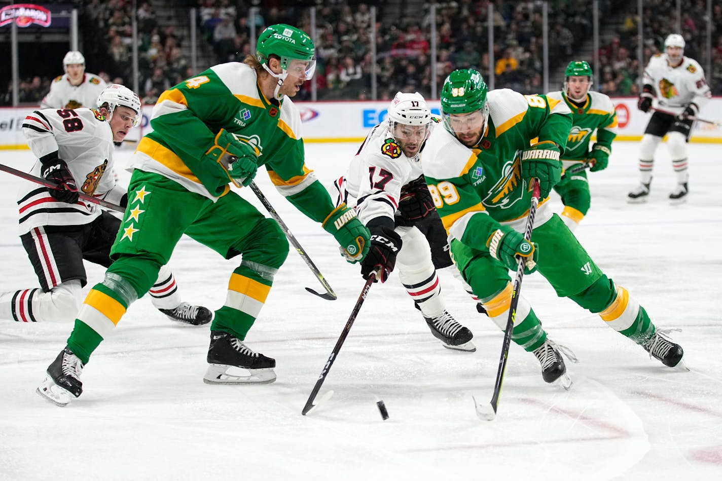 Chicago Blackhawks' Jason Dickinson (17) reaches for the puck against Minnesota Wild defenseman Jon Merrill (4), front left, and center Frederick Gaudreau (89) during the second period of an NHL hockey game Friday, Dec. 16, 2022, in St. Paul, Minn. (AP Photo/Abbie Parr)