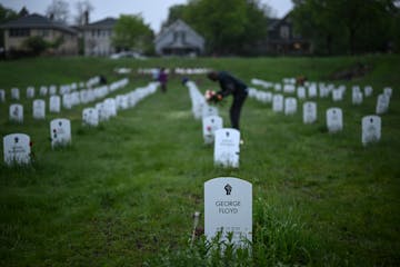 Community members lay flowers down near gravestone markers at the 'Say Their Name' cemetery.