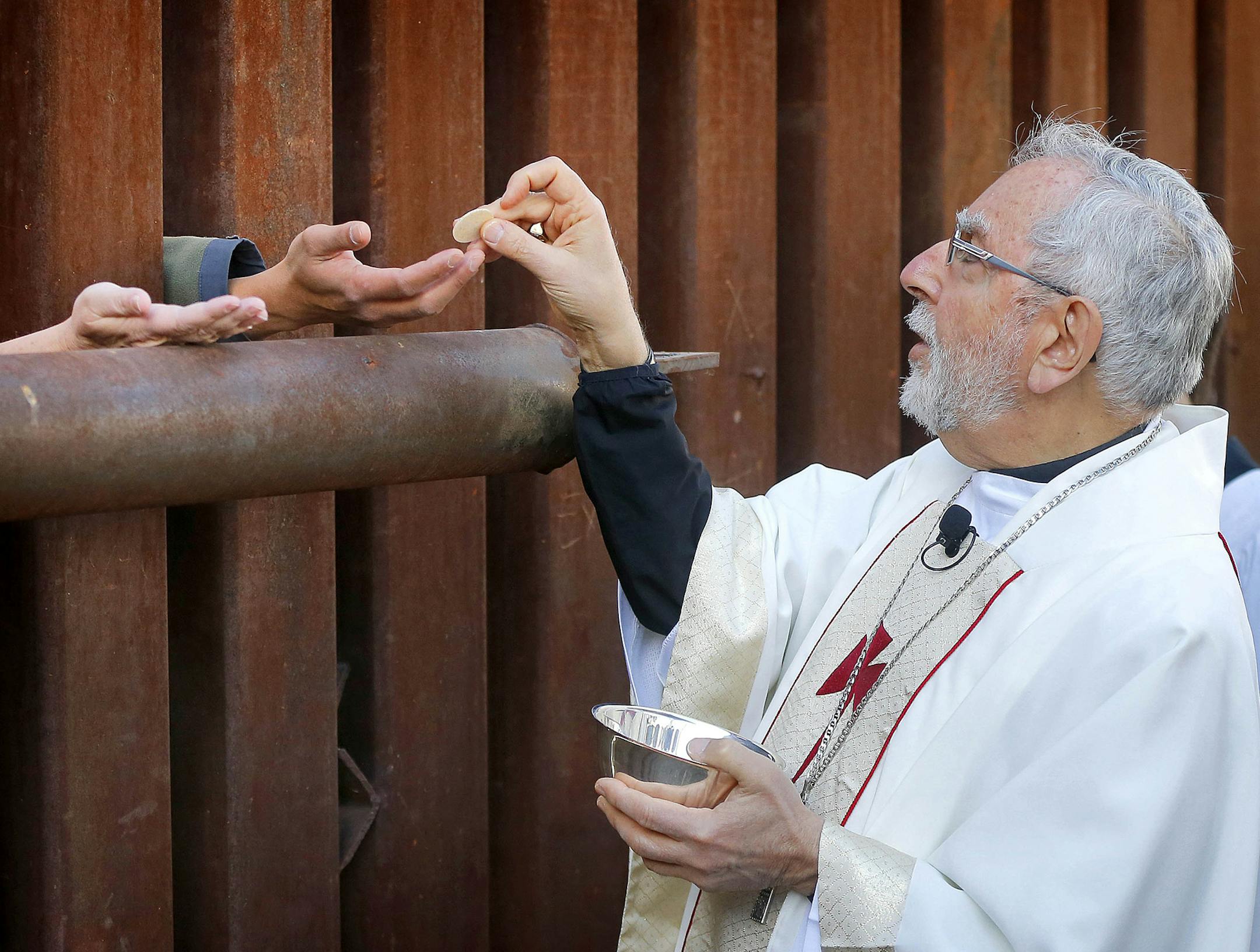Most Reverend Gerald F. Kicanas, Bishop of Tucson, offers communion to people on the Mexican side of the international border, Tuesday, April 1, 2014, in Nogales, Ariz. Kicanas and Boston Archdiocese Cardinal Sean O'Malley, along with several Bishops who serve along the U.S./Mexico border, were visiting the border town to bring awareness to immigration reform and to remember those who have died trying to cross the border in years past. (AP Photo/Matt York) ORG XMIT: MIN2014040118305671
