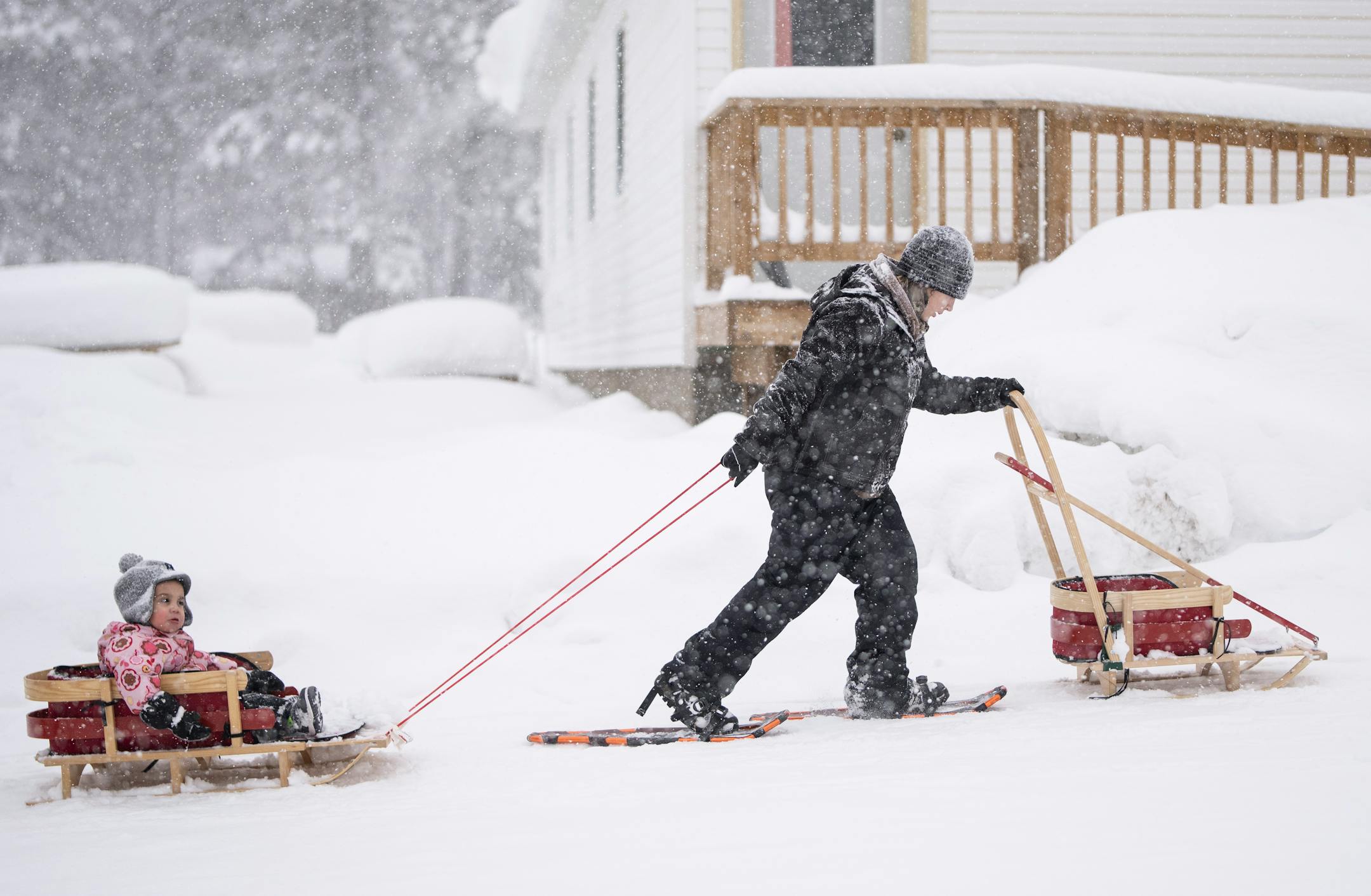 Friends, Family and Neighbor intern Niizhoodewii Denomie walks in snowshoes while dragging Giiwitaa-gizhig Miles Trimble in a sled with a group of moms and children as they check on rabbit snares as part of the Ojibwe immersion program.