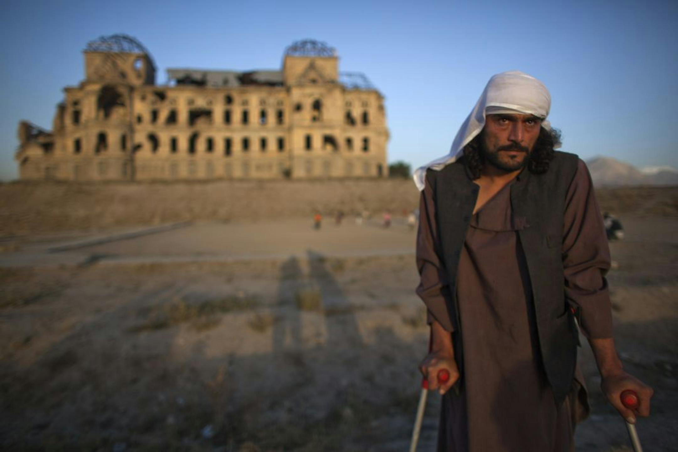 Wahidullah, 32, was crippled during the Afghan civil war in the 1990s. The dilapidated palace behind him in Kabul is a reminder of that war's horror, when rival factions turned their guns on each other.