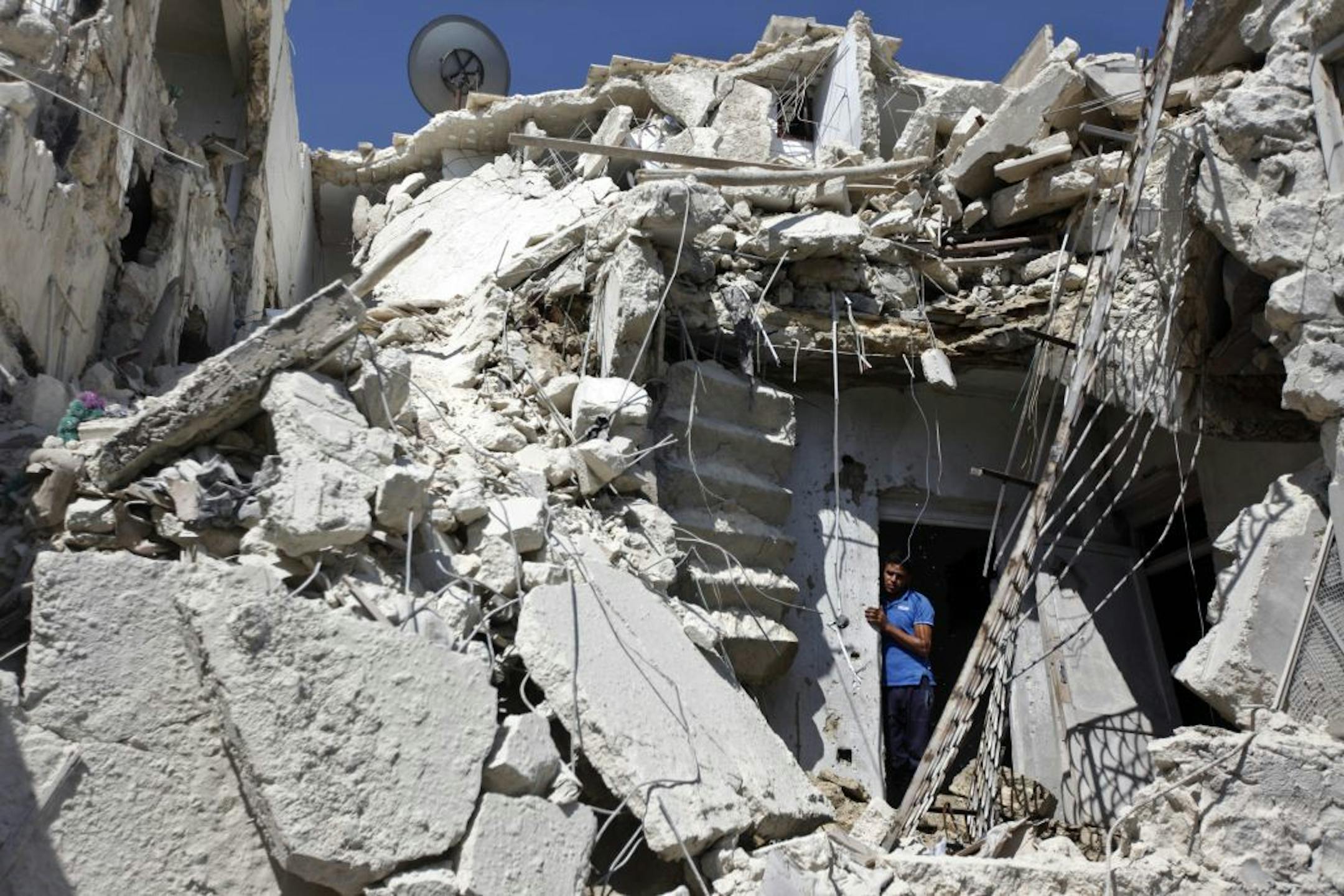 A Syrian man looks out of the rubble as rescuers, not shown, look for the bodies of two girls thought to be under the rubble of a building hit by a Syrian government airstrike in Aleppo, Syria, Sunday, Aug. 19, 2012