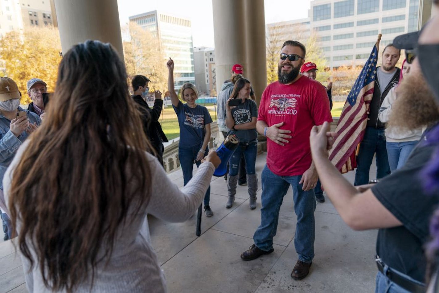 Biden supporter Ani Aikens, left, handed the megaphone to Trump supporter Adam Heikkila, center, during an impromptu civil moderated debate following a protest by Trump supporters over the presidential election results at the State Capitol in Lansing, Mich., Sunday, Nov. 8, 2020.