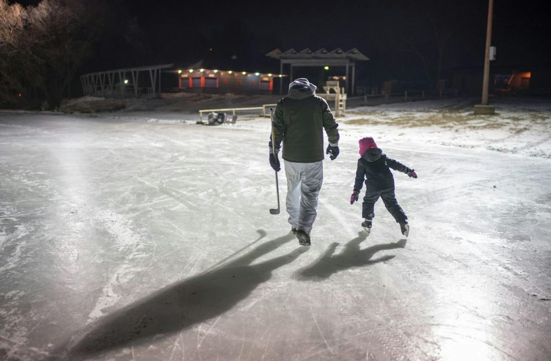 Kendyl Forseth, 7, and her dad, Patrick, headed to the warming house after she kept him company while he dialed in his shot on one of the pond hockey rinks Thursday night. A Fargo native now living in Bentonville, Arkansas, Patrick has played in the tournament with friends he grew up with for the past three years. He and his family always get to town early to sieze the opportunity to visit used sports gear shops to get skates and pads for Kendyl and her brother and their youth hockey teammates b