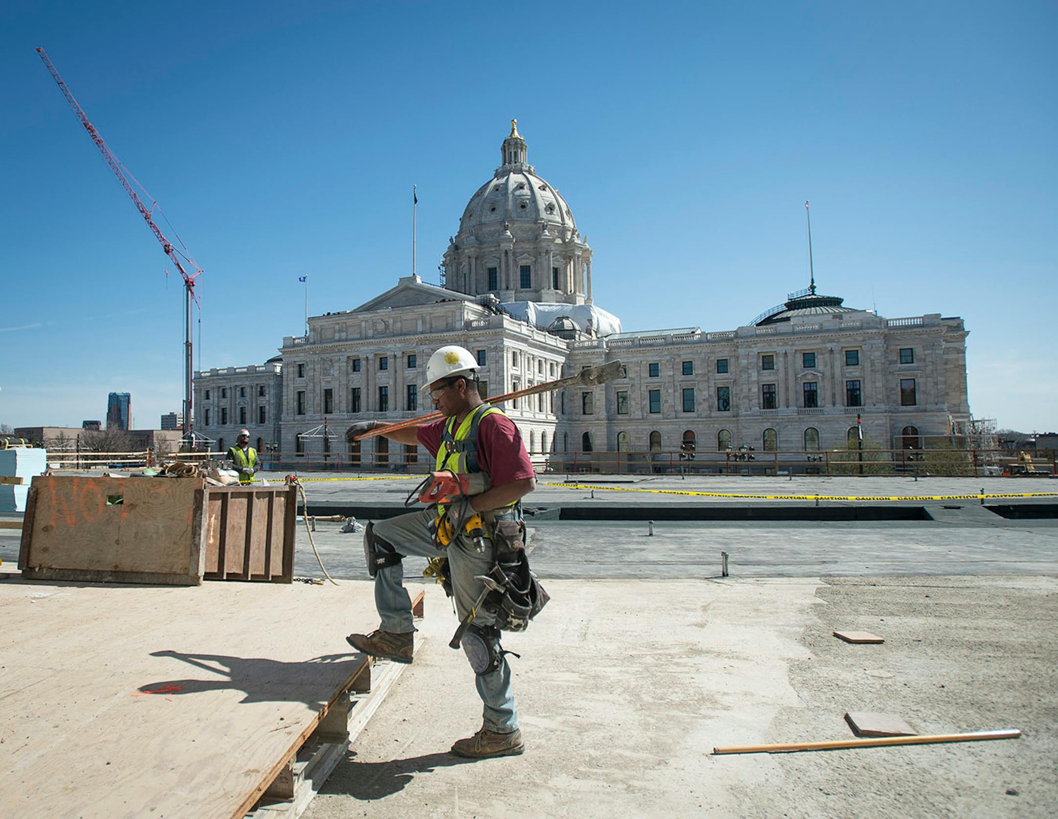 Jerome Flemming, a carpenter, carries a grizzly bar over his shoulder as he walks along the location of a future outdoor plaza at the Senate office building in St. Paul, Minn., Tuesday, April 14, 2015. Senate Democrats included money in a state budget bill this week to start leasing the $90 million facility for its expected opening next year. The tab is $13 million for 2016 and 2017 and about $8 million a year thereafter.