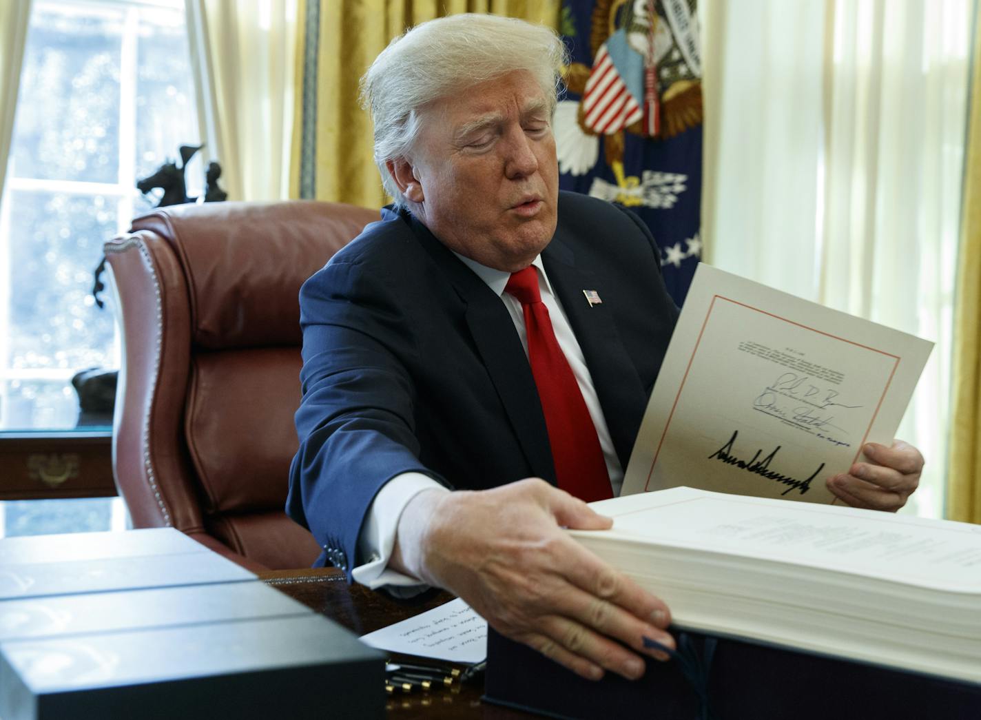 President Donald Trump grabs a box containing the tax bill after signing it in the Oval Office of the White House, Friday, Dec. 22, 2017, in Washington. (AP Photo/Evan Vucci)