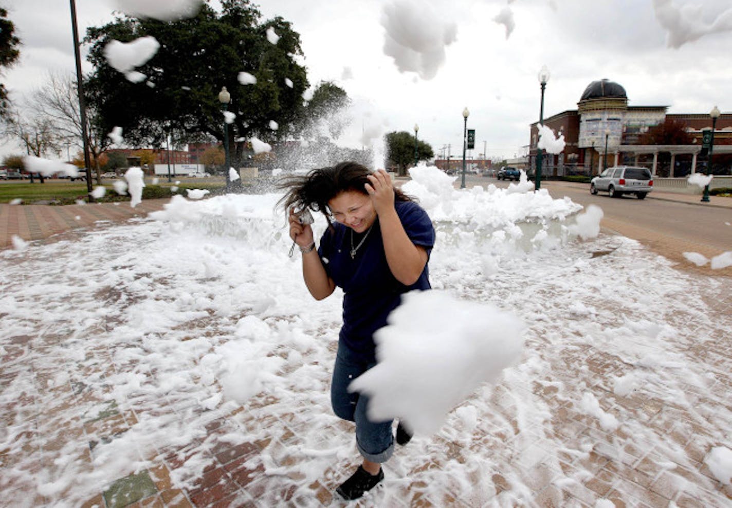 Selena Barrientos, 12, turns away as a gust of wind blows foam in her direction as she tries to take a picture of the Carroll and Frances Sturgis Fountain in front of City Hall in downtown Waco, Texas, Sunday, Jan. 6, 2008. The fountain was the center of a practical joke after bubble bath was added.