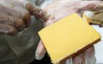 Ken Monteleone, owner of Fromagination, holds a slice of Hook's 20-year cheddar cheese as he talks about the coloring, at his shop on the square in Ma