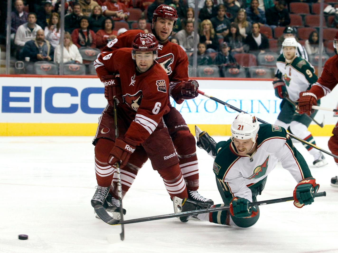 Minnesota Wild center Kyle Brodziak (21) scores on a backhand shot as he is checked to the ice by Phoenix Coyotes defenseman David Schlemko (6) and Derek Morris (53) in the first period of an NHL hockey game, Saturday, Dec. 10, 2011, in Glendale, Ariz. (AP Photo/Paul Connors)