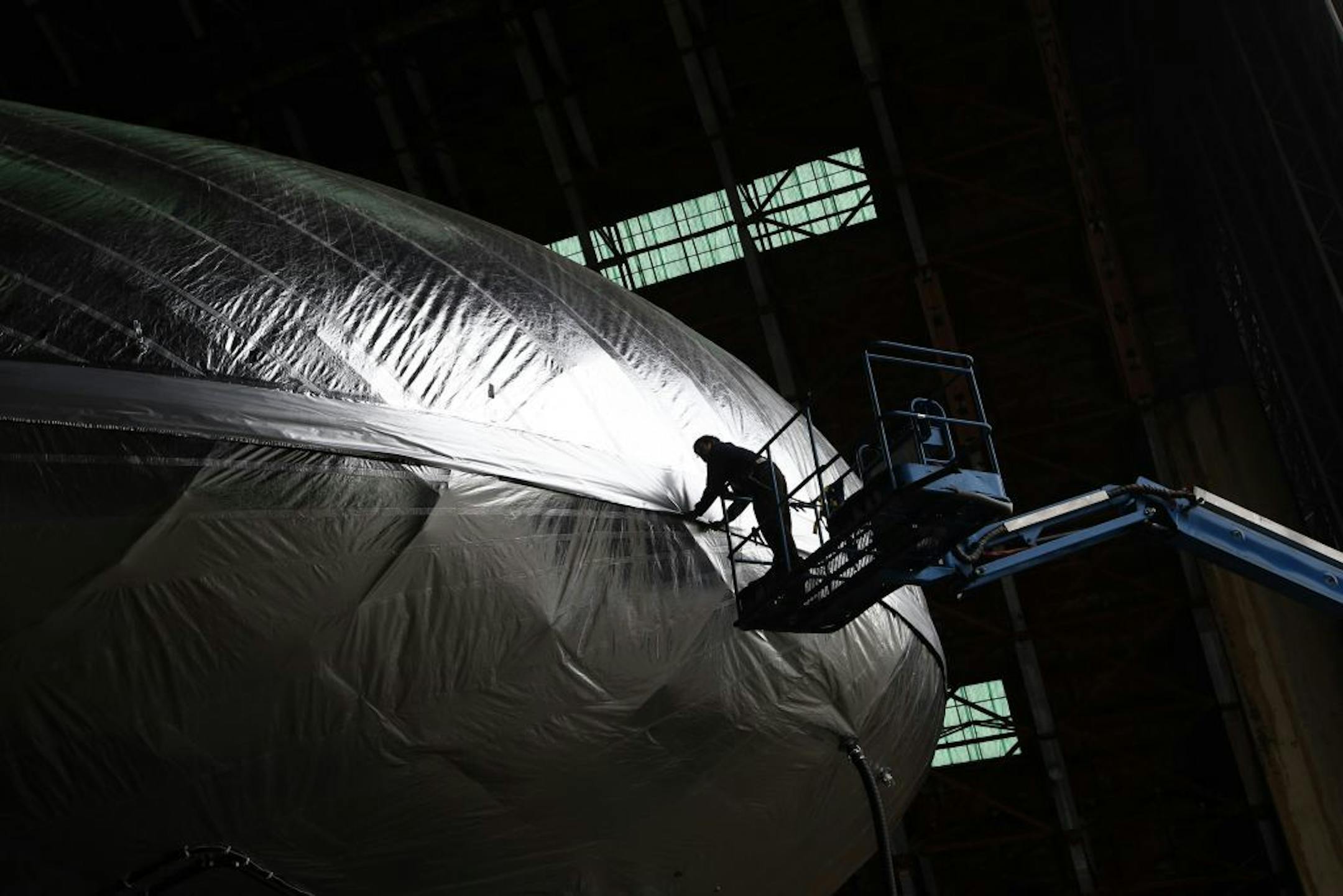 Leonel Cruz pulls down the flab on the Aeroscraft airship, a high-tech prototype airship, in a World War II-era hangar in Tustin, Calif., Thursday, Jan. 24, 2013. Work is almost done on a 230-foot rigid airship inside a blimp hangar at a former military base in Orange Co. The huge cargo-carrying airship is has shiny aluminum skin and a rigid, 230-foot aluminum and carbon fiber skeleton.