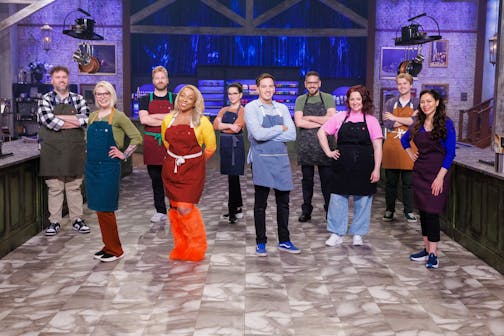 Ten apron-clad chefs stand in a kitchen