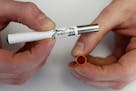 FILE - In this March 2, 2011, file photo, a clerk holds an electronic cigarette and the filter end that holds the liquid nicotine solution at an E-Smo