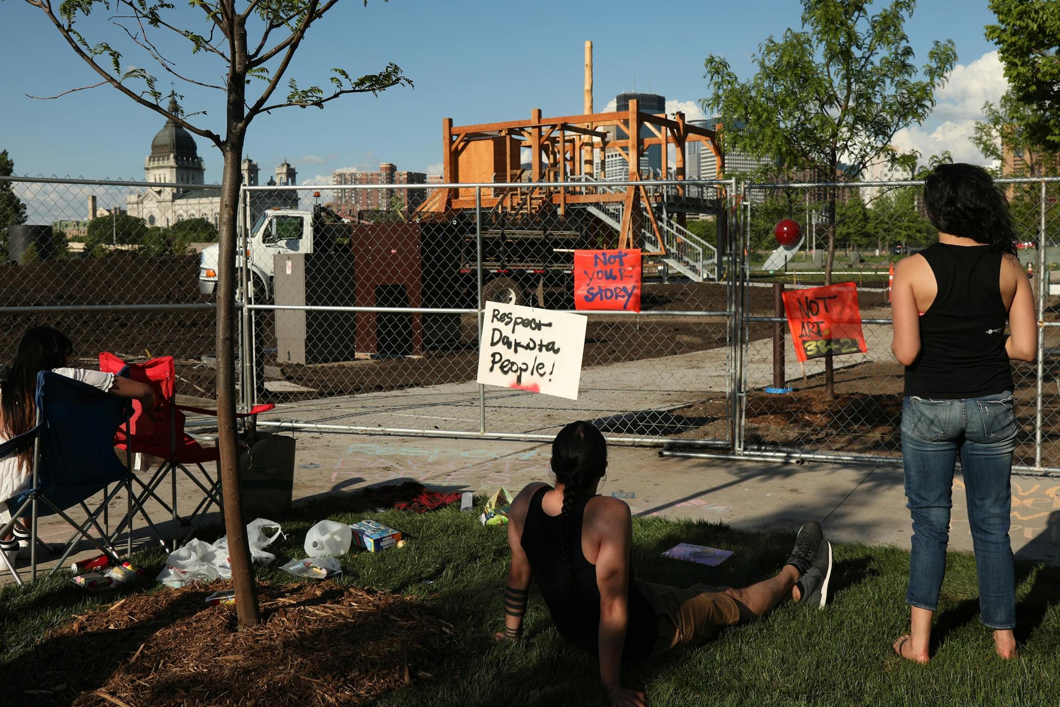 Dakota community members, from left, Graci Horne, Thomas Kenote Jr. and Sasha Huston Brown sat outside the Minneapolis Sculpture Garden protesting "Scaffold" by Sam Durant which depicts the 1867 hangings of 38 Dakota men.