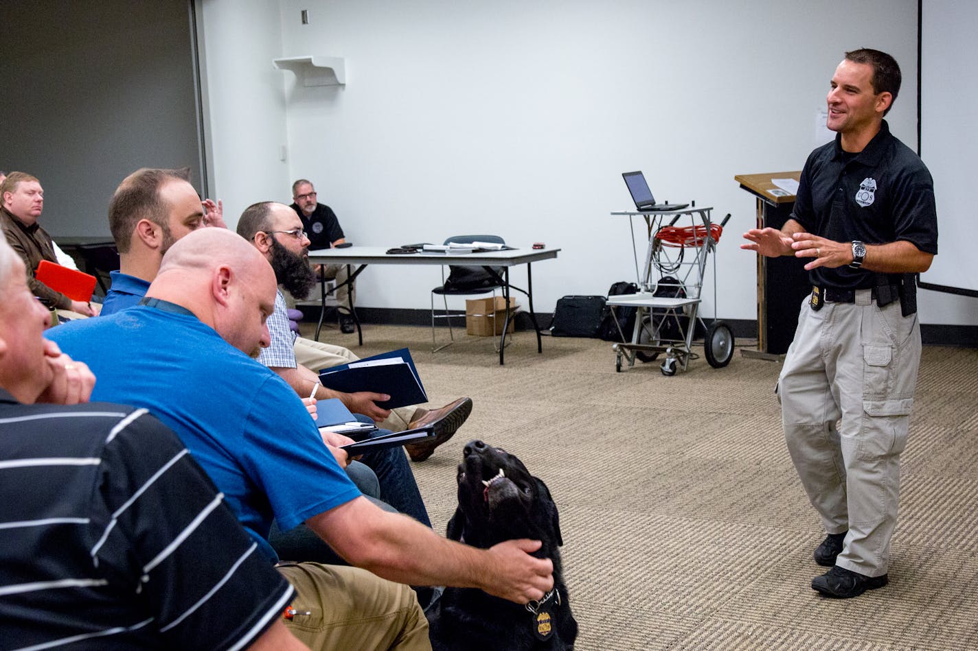 ATF Special Agent Nic Garlie speaks on straw purchasers during the Federal Firearms License Educational Seminar while explosive detection K9 Brock is pet. ] COURTNEY PEDROZA &#x2022; courtney.pedroza@startribune.com; Federal Firearms License Educational Seminar for gun store owners to protect against crimes like straw purchasing; Hennepin County Library in Edina; July 27, 2017; K9 Brock; explosive detection K9 including firearms, shell casing, and ammo