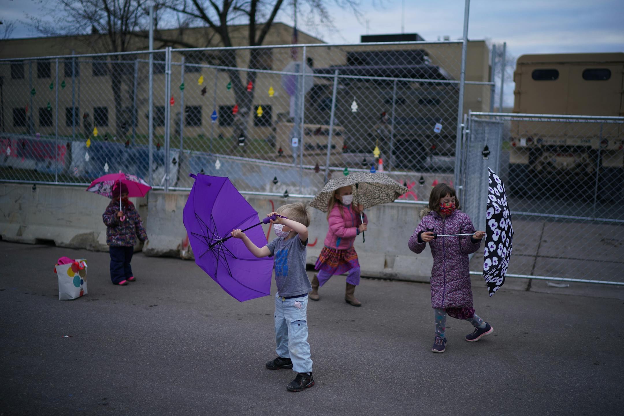 Children played with umbrellas outside the fence surrounding the Brooklyn Center Police Department while their parents were near.