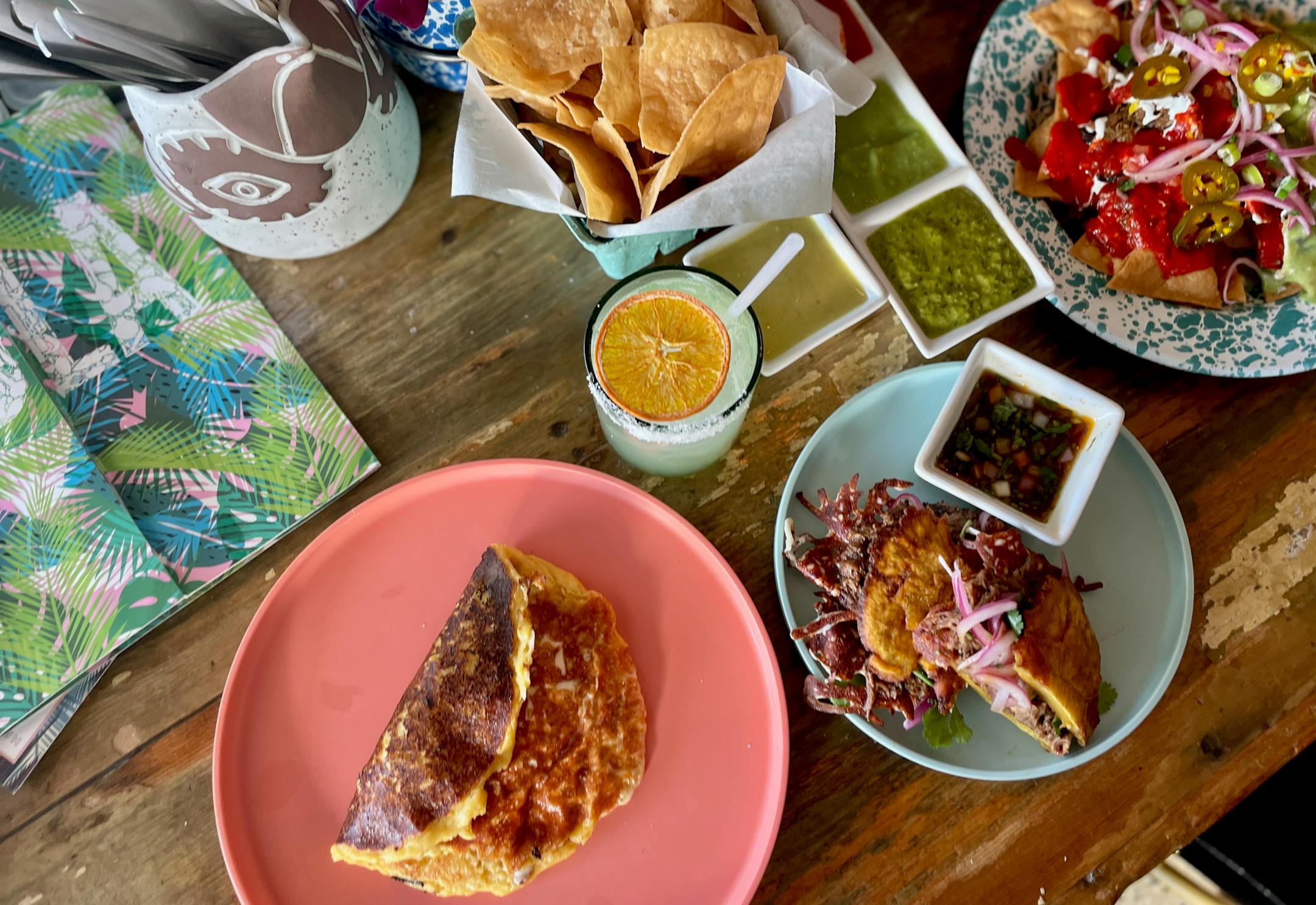 The bar at Hola Arepa filled with new happy hour food: quesabirria on a tostone, corn pancake, nachos and chips and salsa. March 12, 2024