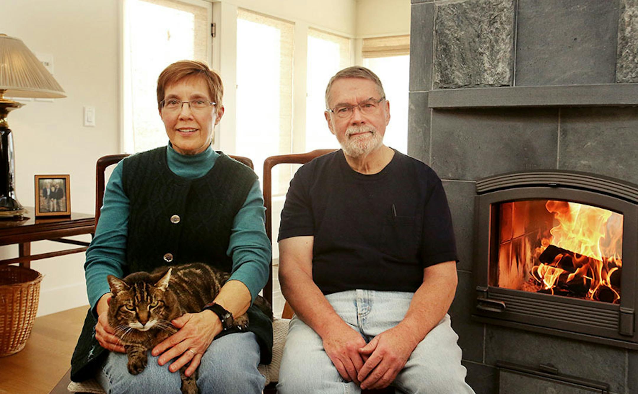 Susan and Jeff Saffle's passion for birdwatching and nature drove the design of this Scandinavian version of a Prairie Modern home in Lake Elmo by Rehkamp Larson Architects. Here, Jeff and Susan Saffle sit with their cat Frank, next to their Finnish Tulikivi stove and fireplace which utilizes soapstone to retain radiant heat from the fire to produce comfort, warmth and efficiency Wednesday, Jan. 13, 2016, in Lake Elmo, MN.