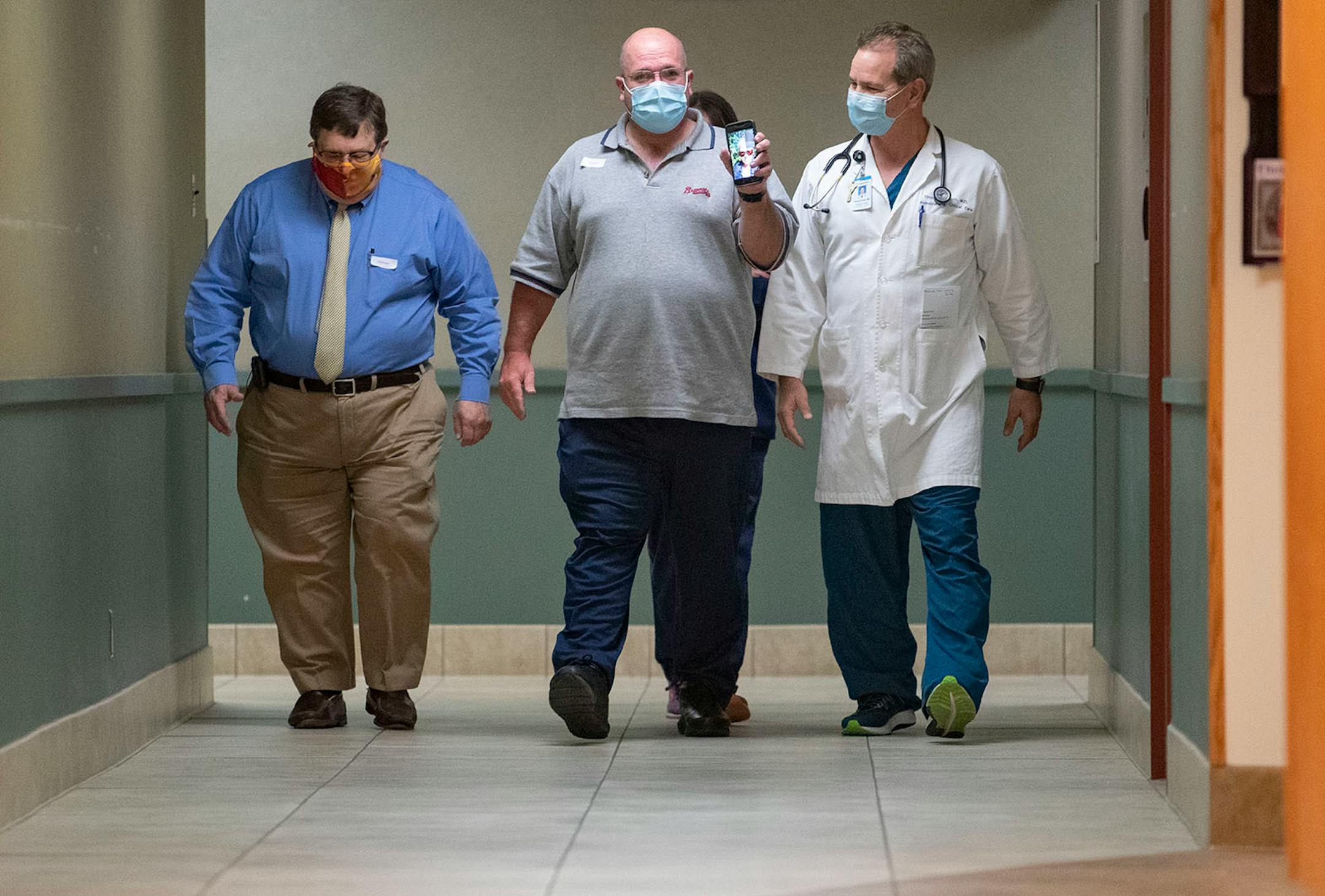 Tim White held up his phone while facetiming his sister, Mary Ellen Evangelista and was flanked by (left) Dr. David Ingbar, M.D. from the University of Minnesota and Dr. Tim Rich, M.D. from Essentia Health while walking down the hall to meet the only other person in the world to receive the same experimental ARDS treatment as him. The meeting took place at Essentia Health-St. Mary's Medical Center in Duluth on Friday October 16, 2020.