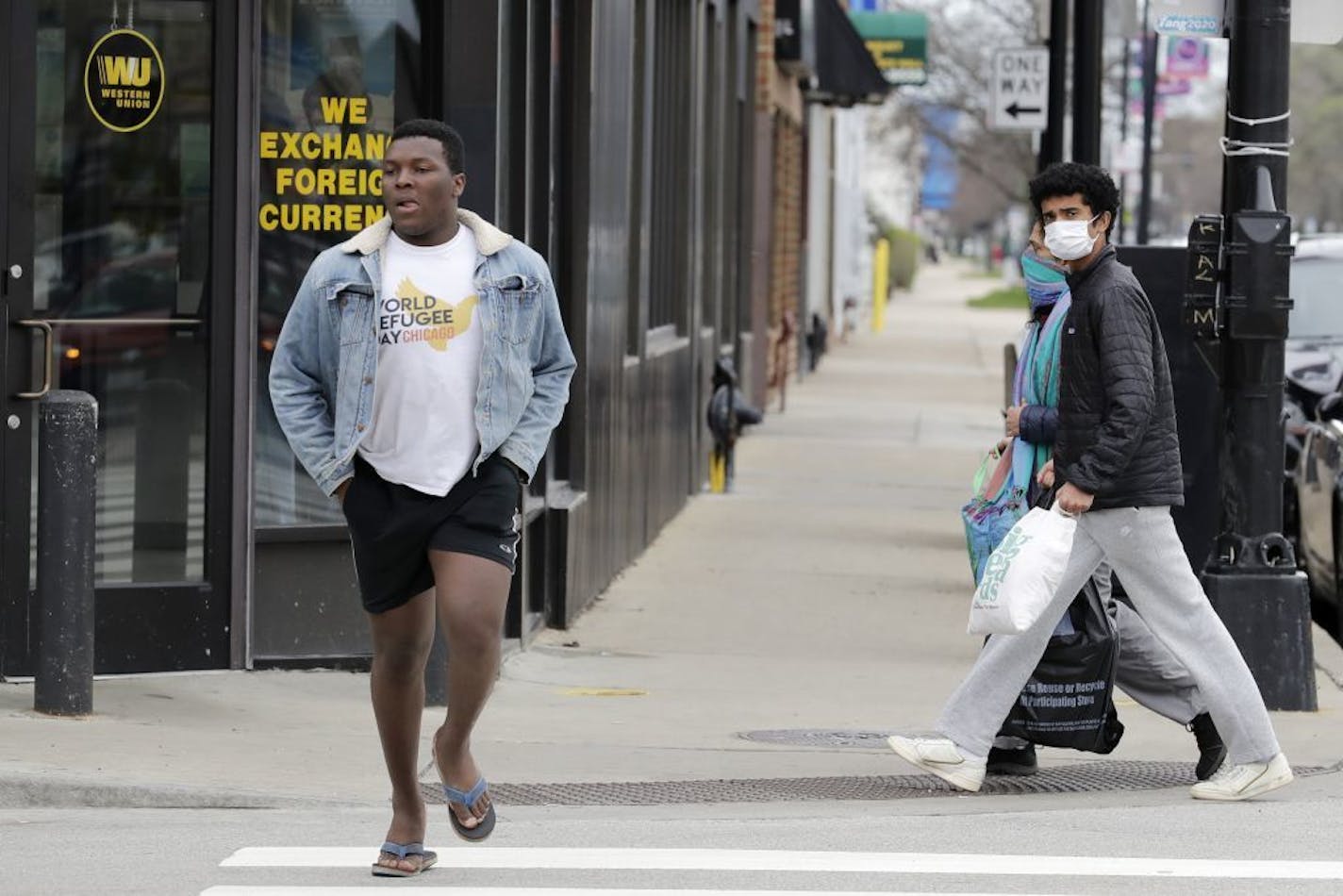 People, right, wear mask as they look to a man crosses the street without a mask during the COVID-19 in Chicago, Thursday, April 30, 2020. New Illinois rules about wearing a face mask over age 2 start Friday, May 1, when they can't maintain a 6 foot social distance in public.