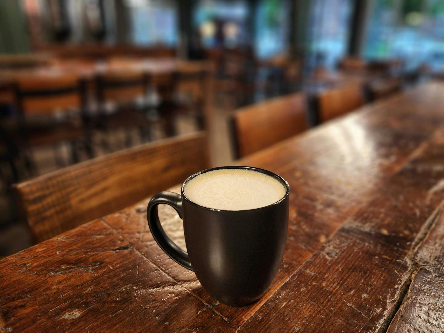 A black mug filled with a white liquid, set on a dark wooden table