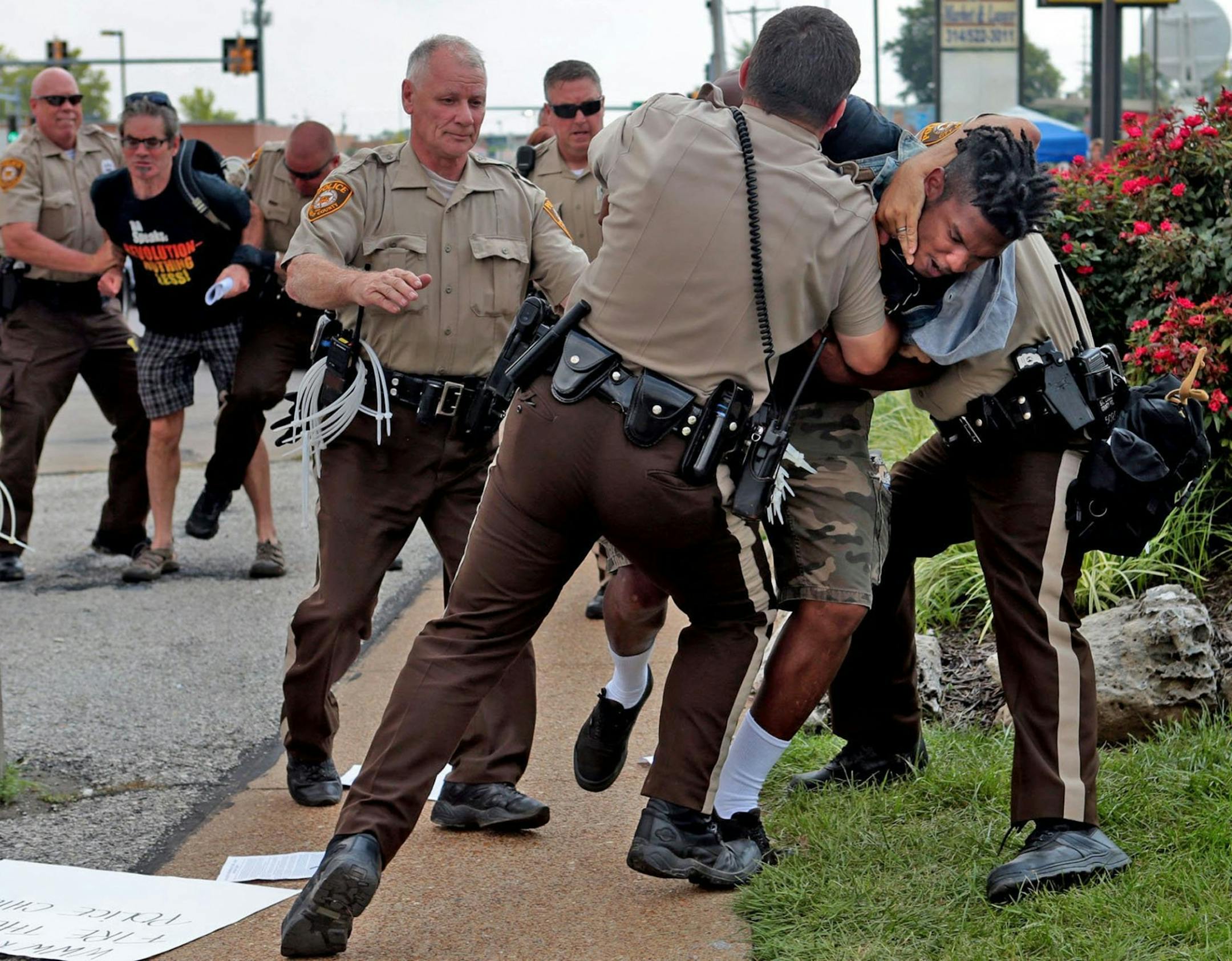 Police tackle a man who was walking down the street in front of McDonald's on Monday, Aug. 18, 2014, in Ferguson, Mo. The man appeared to be walking past a group that had been assembled nearby and police were telling everyone to keep walking. Moments after he turned around and exchanged words with the police that he was just walking, police took him to the ground. Although there is no curfew in order tonight, police are strictly enforcing protestors to keep moving along the sidewalk or they are