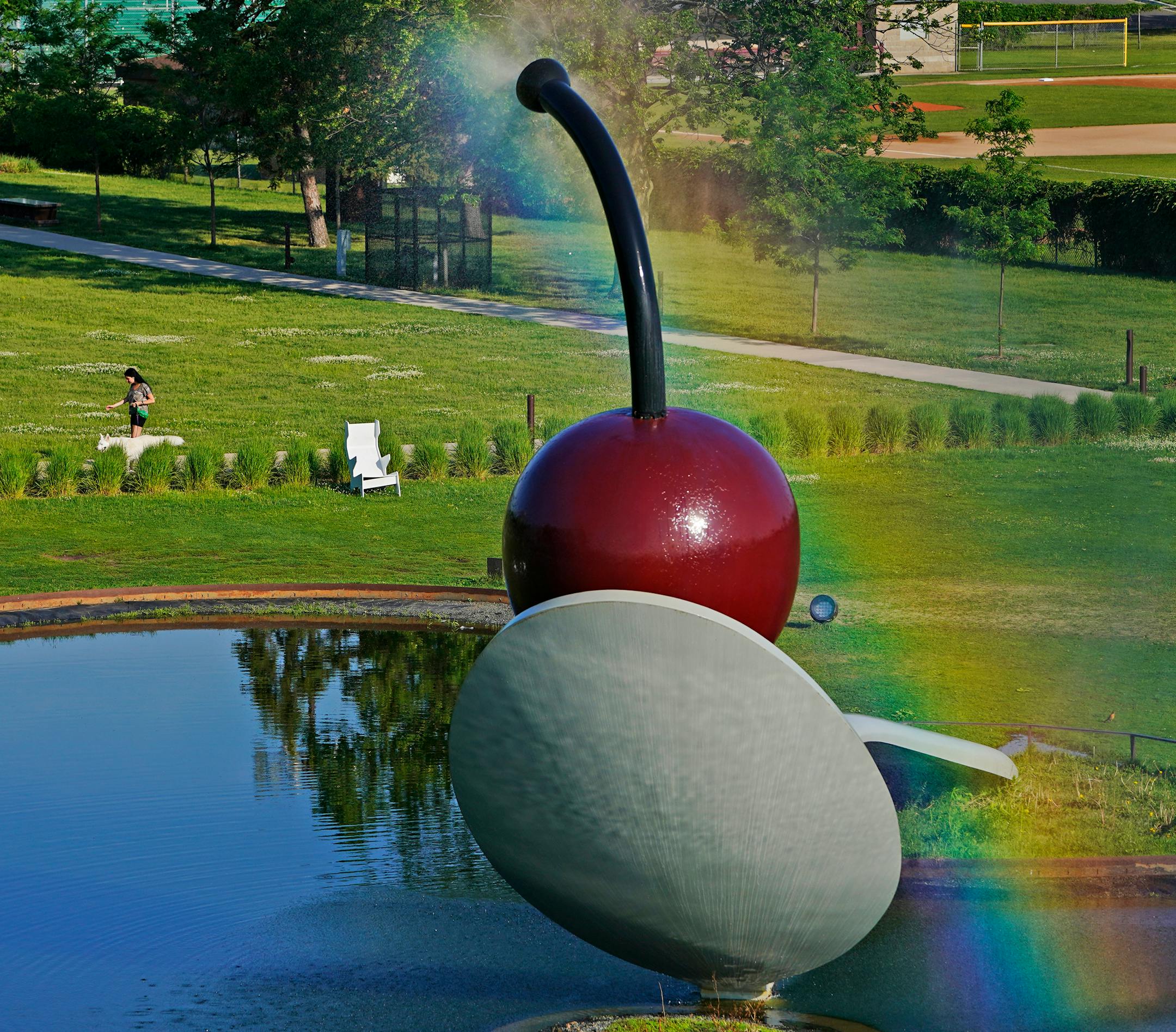 Intense morning sun rays create a rainbow over water spray coming from the "Spoonbridge and Cherry" sculpture on June 7, 2021.