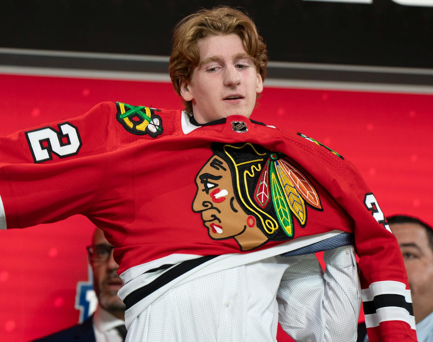 The Chicago Blackhawks' 25th pick, Sam Rinzel, puts on his jersey during the first round of the NHL hockey draft Thursday, July 7, 2022, in Montreal. (Ryan Remiorz/The Canadian Press via AP)