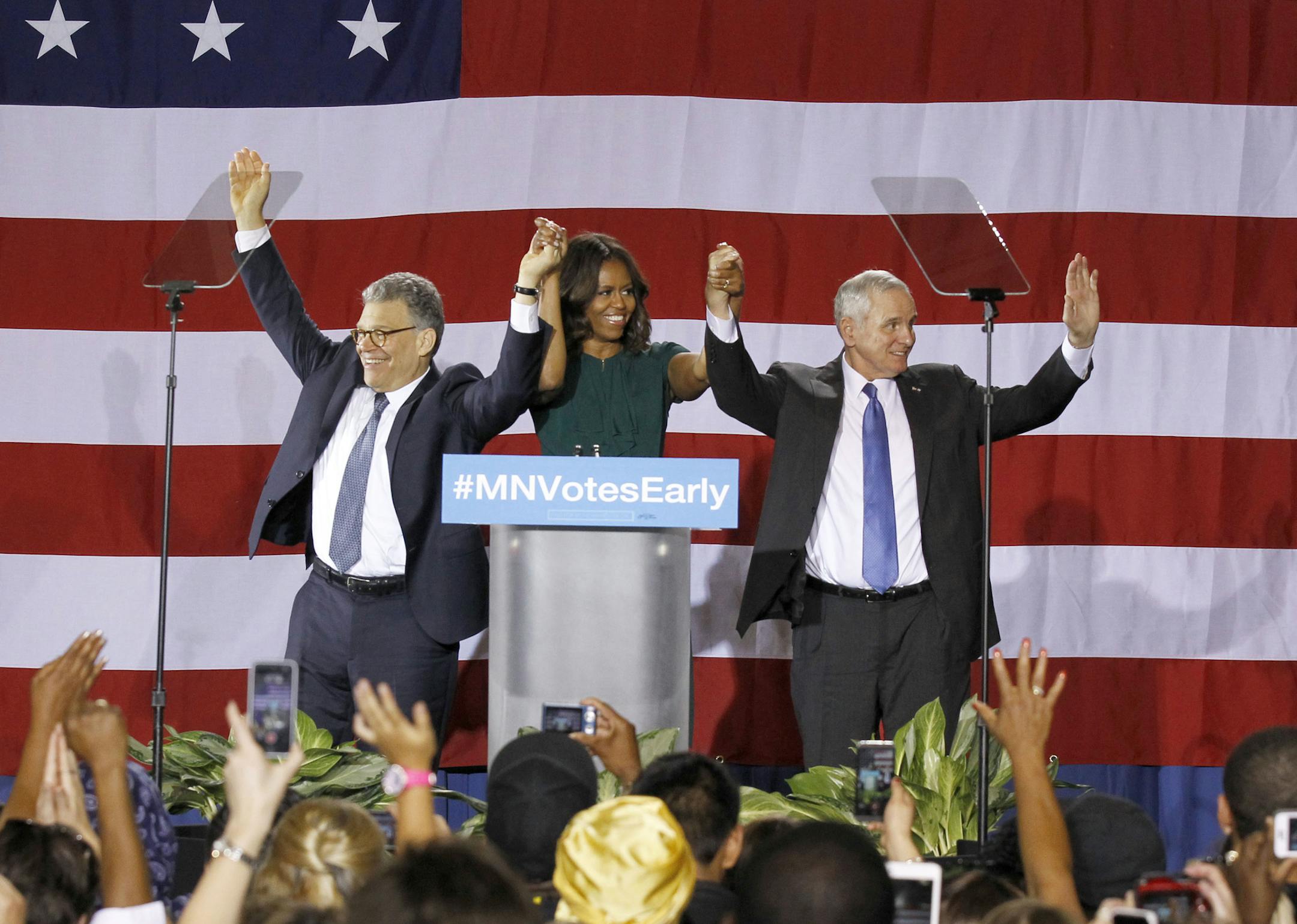 First lady Michelle Obama, center, joins Democratic U.S. Sen. Al Franken, left, and Minnesota Democratic Gov. Mark Dayton, right, at a get-out-the-vote rally at Patrick Henry High School in Minneapolis, Tuesday, Oct. 21, 2014. (AP Photo/Ann Heisenfelt) ORG XMIT: MIN2014102119184453