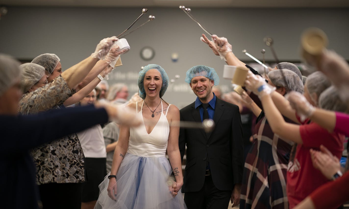 Newlyweds Chara Juneau and Adam Claude walked under a canopy of scoops and measuring cups held by their guests after the couple's wedding at the food packaging warehouse.