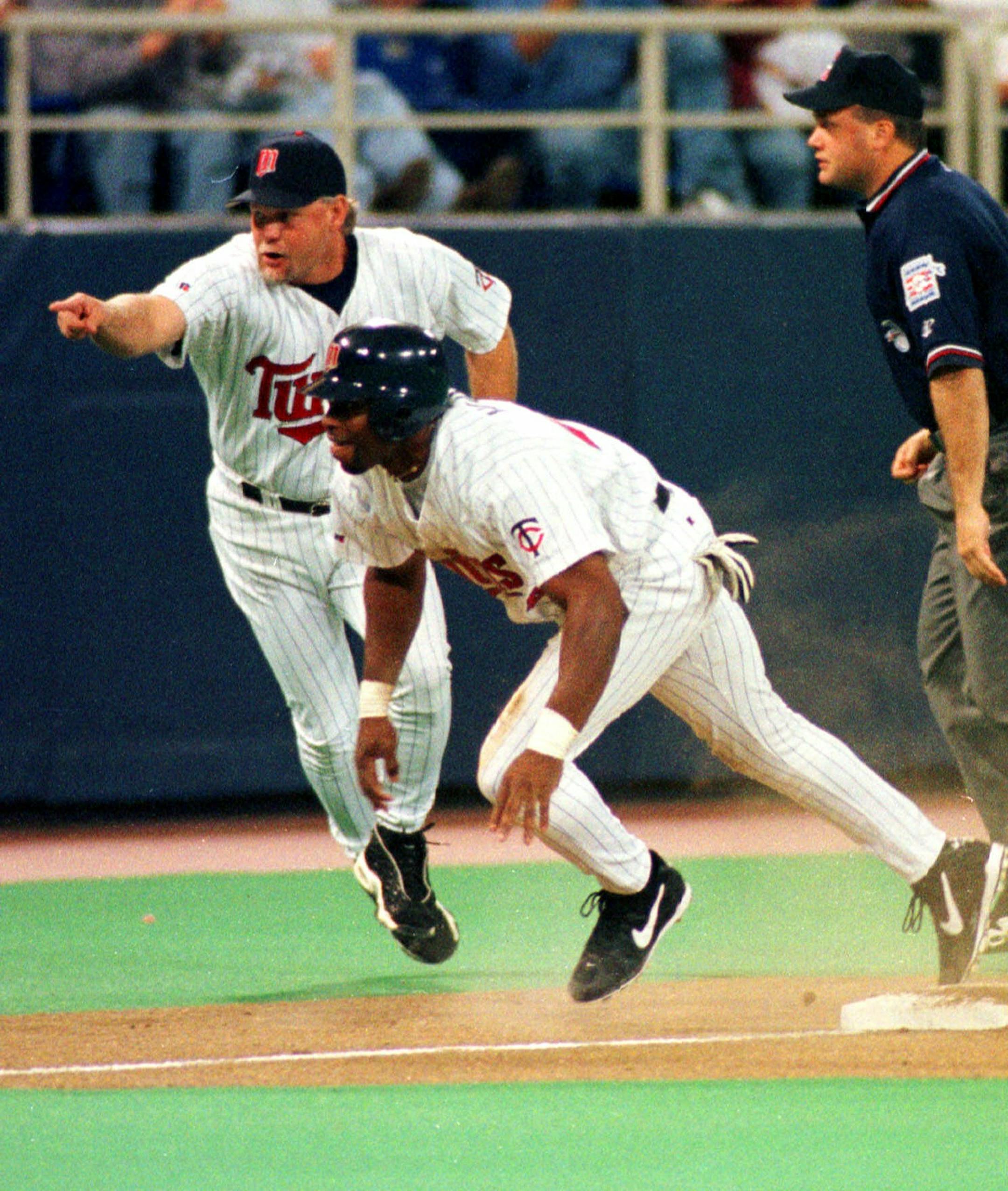 Minnesota Twins third base coach Ron Gardenhire, left, goes airborne as he points the way home to Torii Hunter who scores after a throw out attempt at third failed and the ball got past Seattle Mariners third baseman Russ Davis in first inning Tuesday, May 25, 1999 in Minneapolis. At right is umpire Brian O'Nora. (AP Photo/Jim Mone)