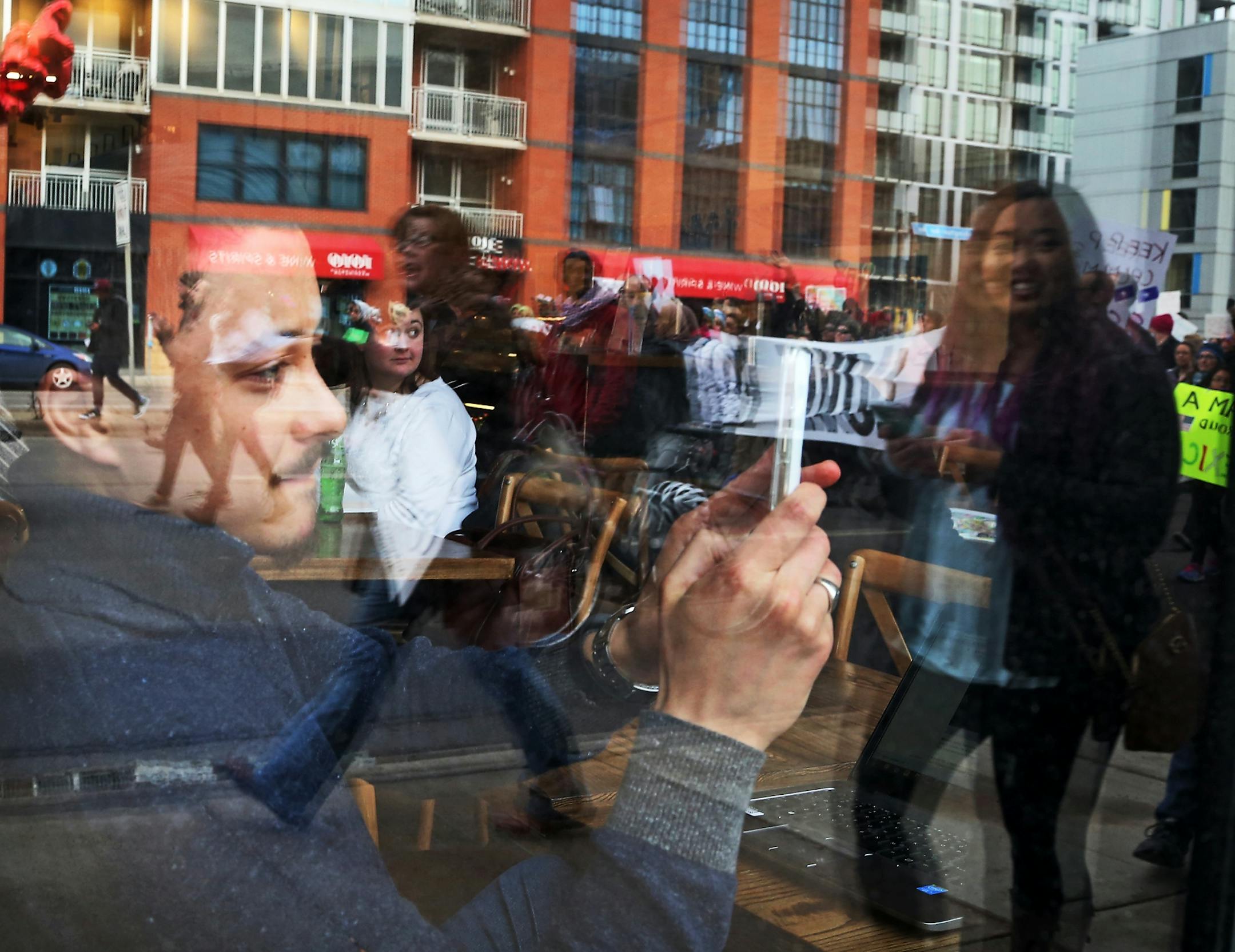An onlooker takes in the scene of The Caravan of Love: A Walk of Love for Immigrants and Refugees as it passes near a book store and cafe near the Cedar-Riverside neighborhood.