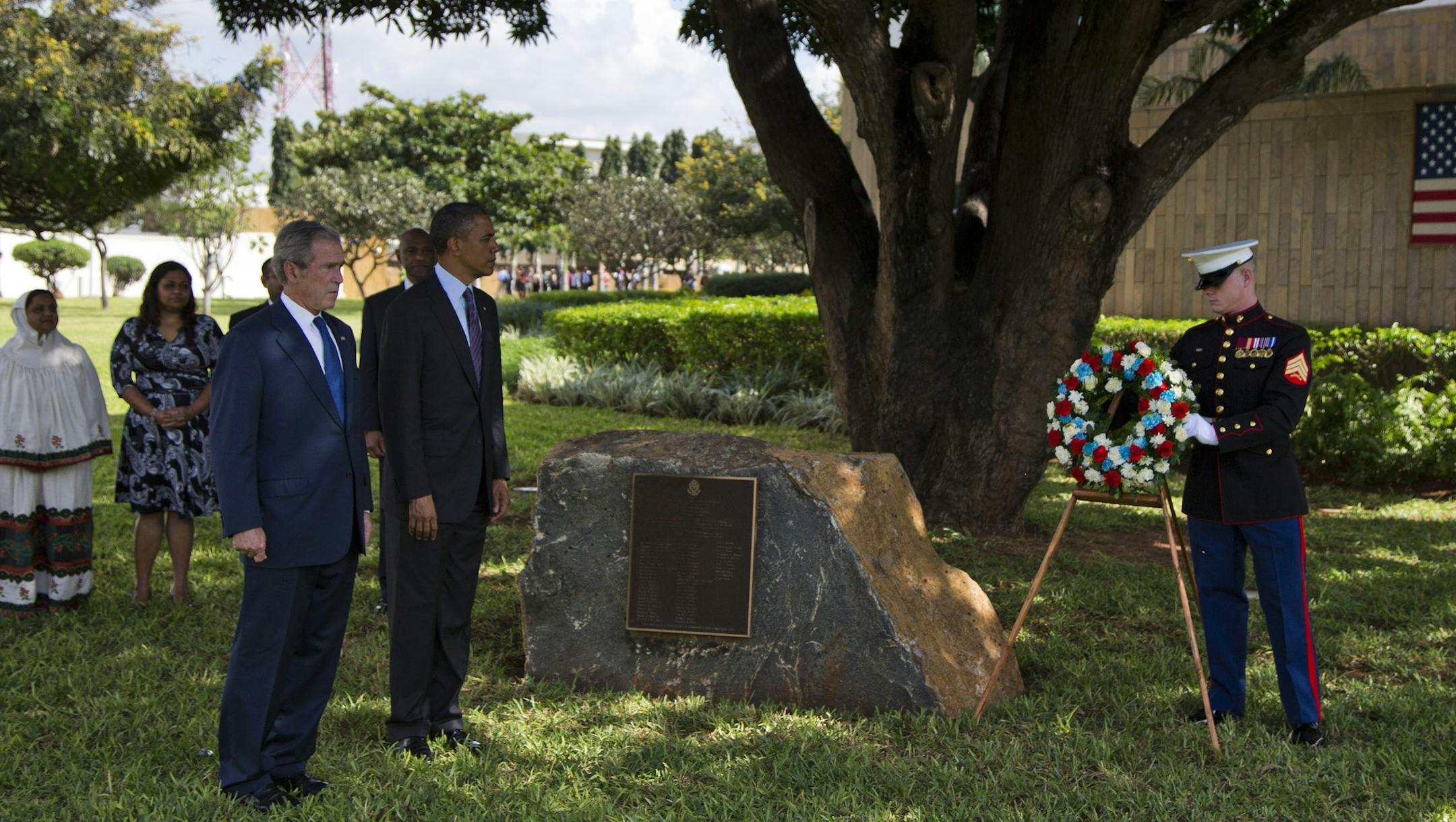 U.S. President Barack Obama and former U.S. president George W. Bush as a Marine places a wreath to honor the victims of the U.S. embassy bombing on Tuesday, July 2, 2013, in Dar Es Salaam, Tanzania. The president is traveling in Tanzania on the final leg of his three-country tour in Africa. (AP Photo/Evan Vucci)