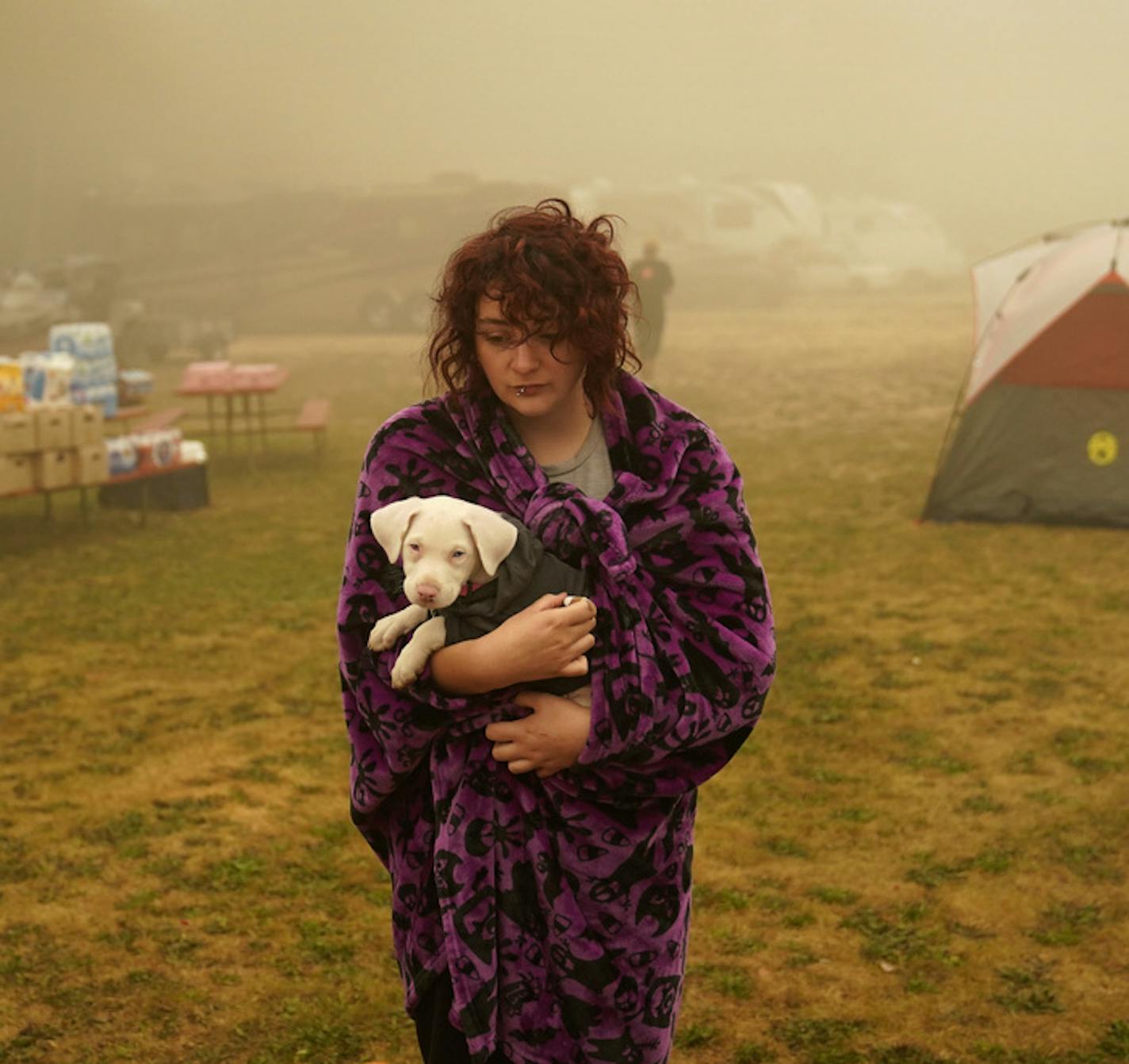 Shayanne Summers holds her dog Toph while wrapped in a blanket after several days of staying in a tent at an evacuation center at the Milwaukie-Portland Elks Lodge, Sunday, Sept. 13, 2020, in Oak Grove, Ore. "It's nice enough here you could almost think of this as camping and forget everything else, almost," said Summers about staying at the center after evacuating from near Molalla, Oregon which was threatened by the Riverside Fire. (AP Photo/John Locher)