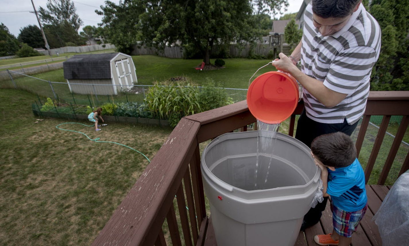 Teddy Cuellar, 4, watched his father, Matt, pour water from the shower into a rain barrel at their Cottage Grove home last week. The city had shut down several wells and imposed a watering ban, which was lifted Tuesday.