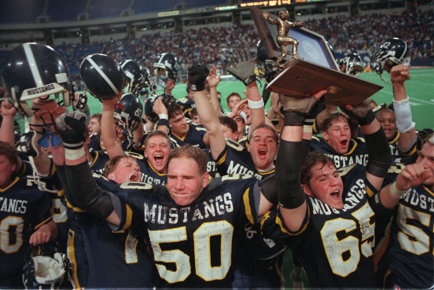 Michael Boosalis, #65, raises Breck's state championship trophy in the air as the team celebrates their class B victory over Windom Area Friday night at the Metrodome.