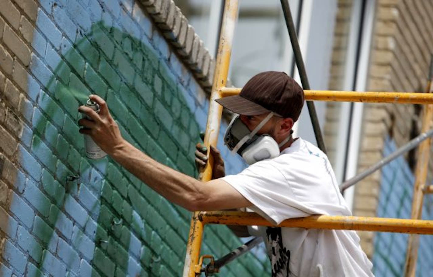 Local graffiti artist Eric Franzen paints a mural on the back of the Pinnacle Building during the Art A Whirl weekend. Franzen, 28, will have about 25 hours in his painting and use more than 20 cans of spray paint once it is finished., He describes his piece as in the graffiti style but without letters.