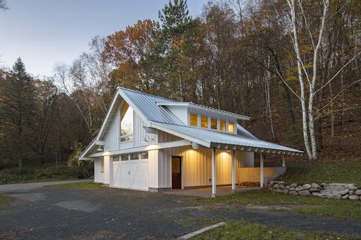 The low-slung structure is nestled into a hill and duo “side wings” span out from a steep-pitched gable. Shed dormers create additional space and draw light into the upstairs loft.