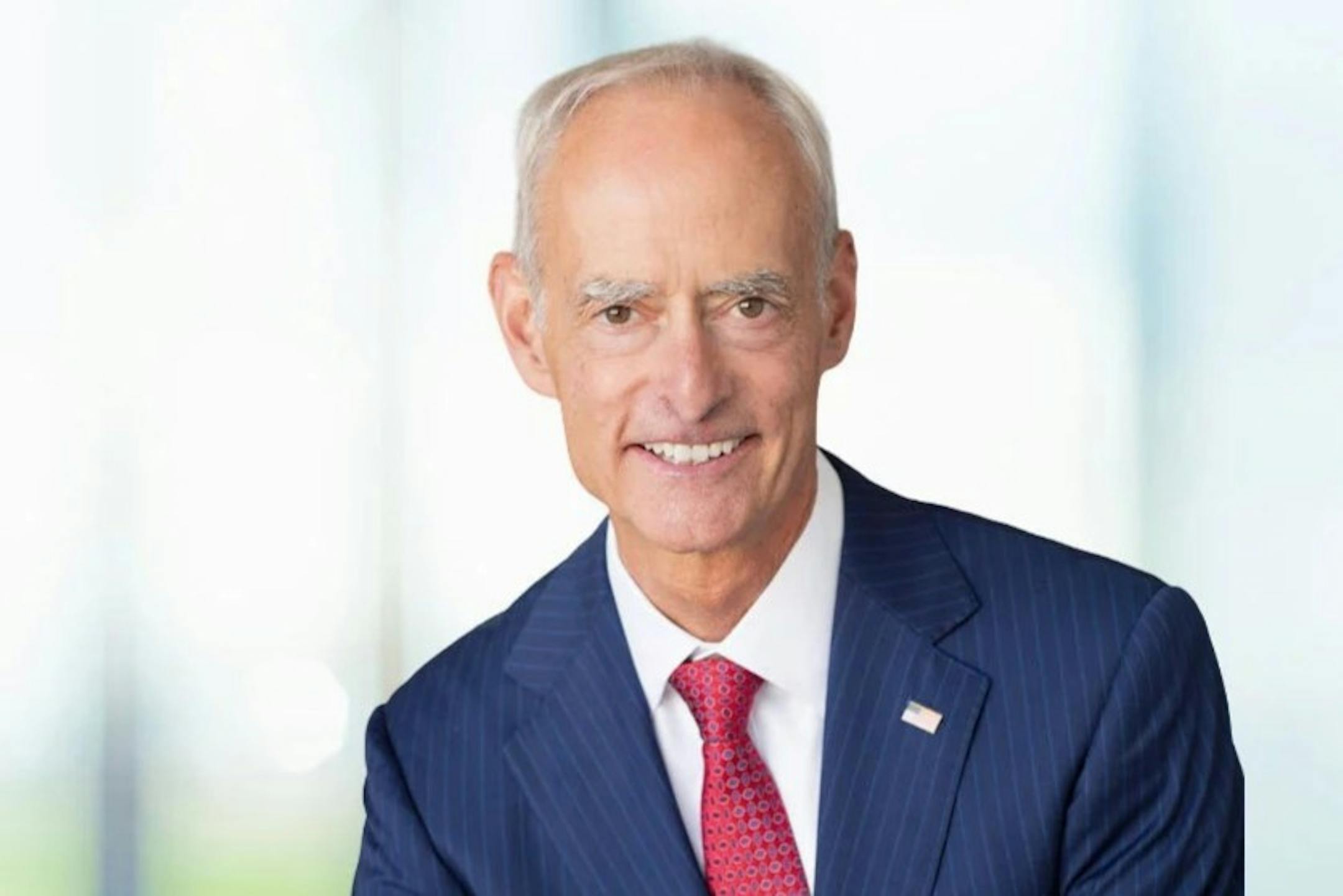 Ron Schutz in blue striped suit, white shirt, red patterned tie and flag pin.