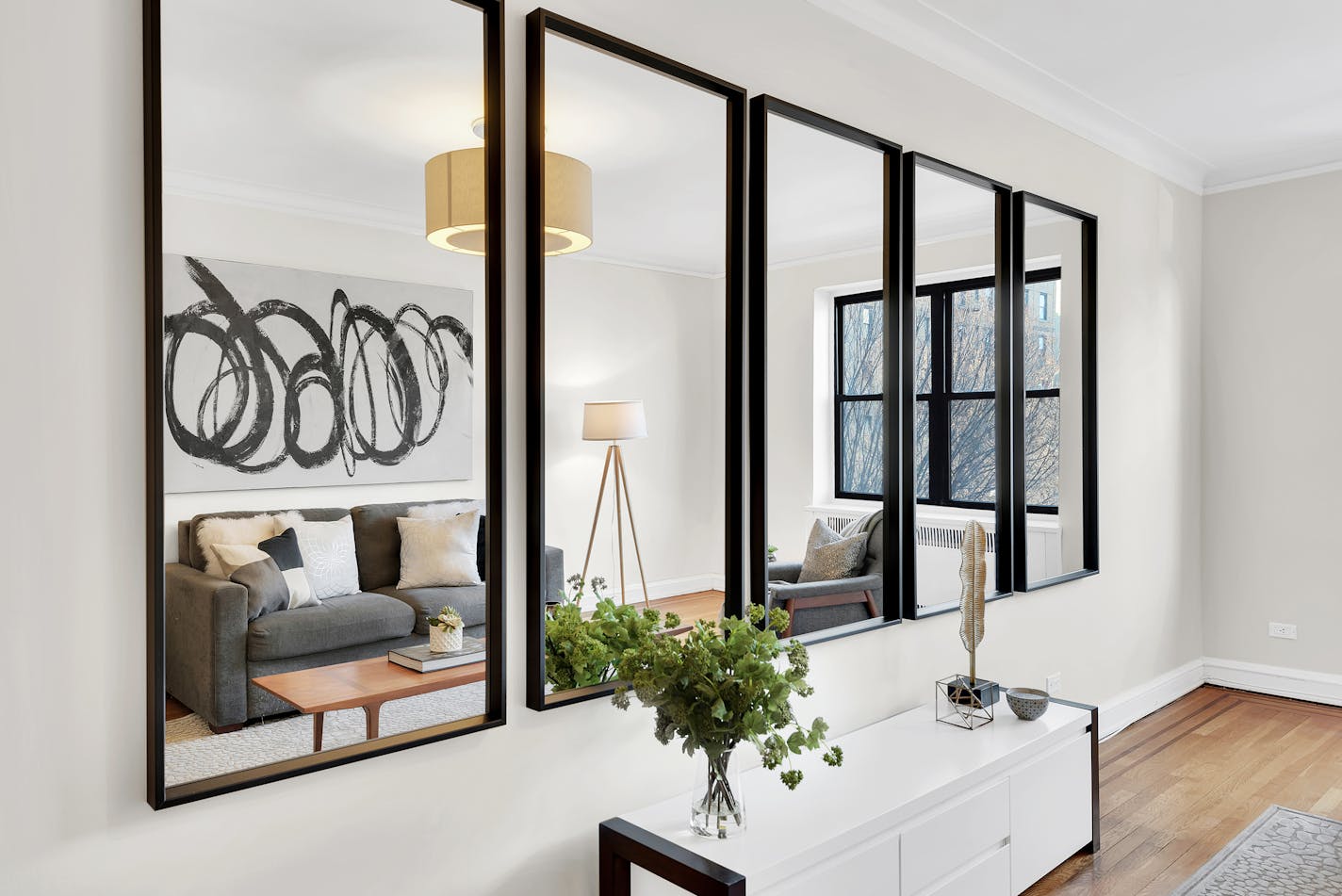 A row of five vertical mirrors with black frames on a white wall reflects a living room.