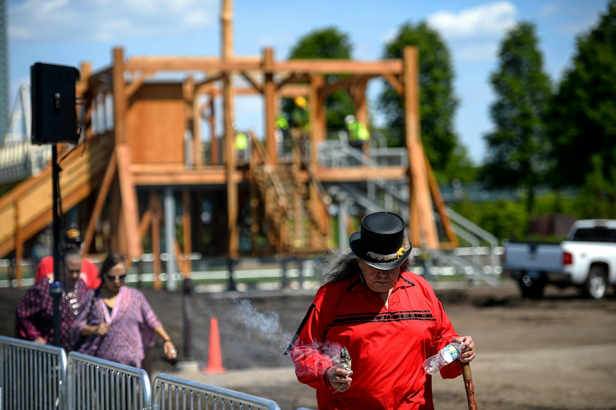 Joseph Bester, the spiritual person for the Mendota Dakota, center, walked away from the "Scaffold" sculpture while burning sage as the dismantling of the sculpture took place behind him Friday afternoon.