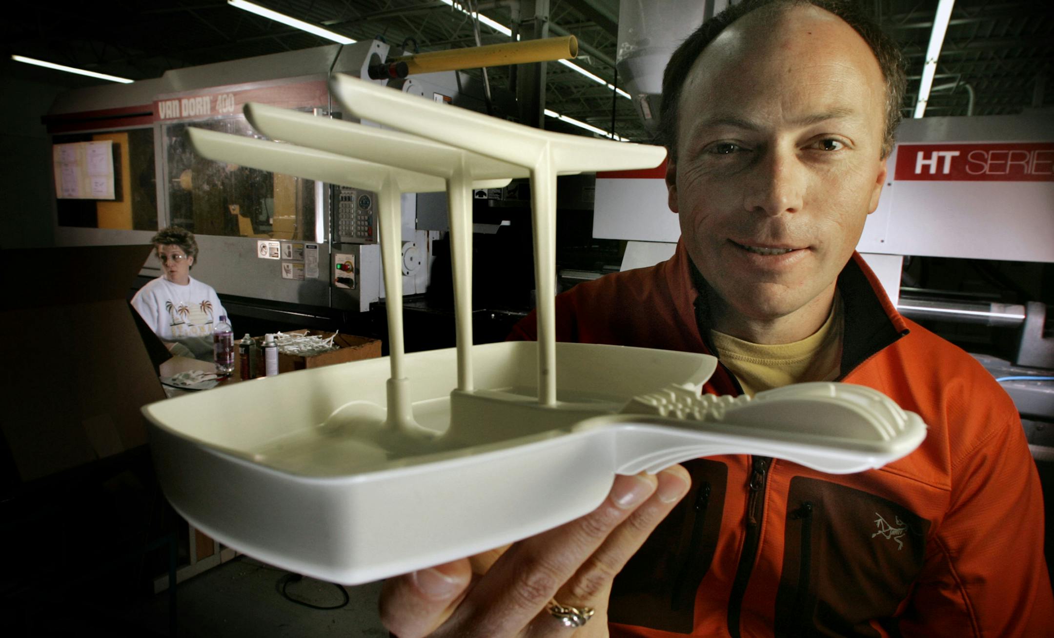 JIM GEHRZ &#xd4; jgehrz@startribune.com St. Croix Falls, WI/March 22, 2006/10:30AM Jonathan Fleck, owner of Makin&#xcc; Bacon in St. Croix Falls, WI., displays one of the small plastic contraptions that is used to cook bacon in a microwave oven. Behind Fleck is the machine used to mold the product and worker Peggy Wittmann.