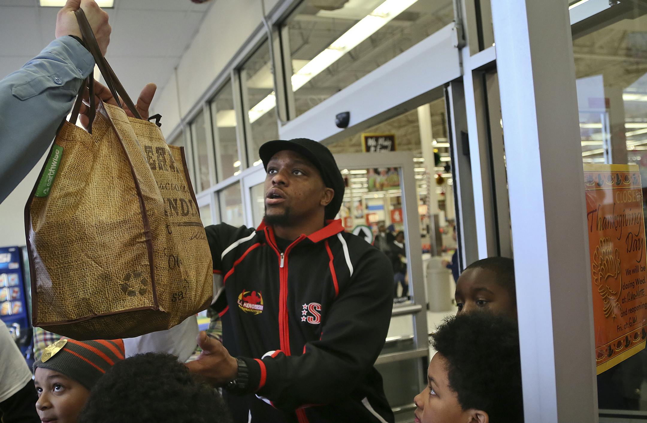 Former Viking E.J. Henderson, along with former Vikings teammates and some current players gathered Tuesday, Nov. 19, 2013, at Cub Foods on West Broadway in north Minneapolis, MN, to help distribute Thanksgiving turkeys and meals to those in need. More than 2,000 turkeys and fixings were handed out. Here, Henderson passes along a bag filled with a turkey and all the fixings so be given out to someone in need. This is the sixth year that Henderson, through his EJ Henderson Youth Foundation, has p