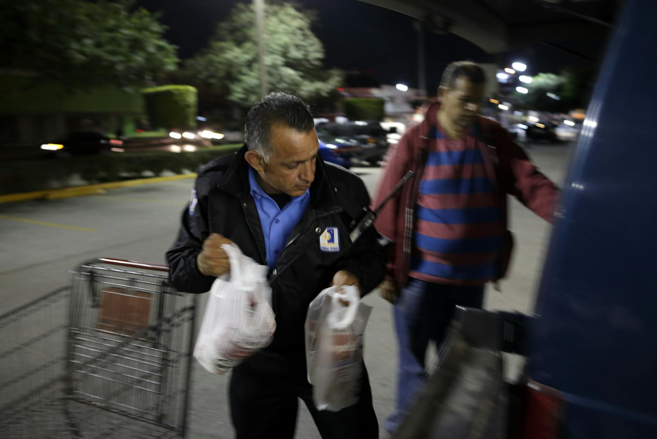 Security guard Guillermo Soria, left, helps a customer while working in front of a Smart & Final store Wednesday, Nov. 18, 2015, in Tijuana, Mexico. After living for nearly 25 years in the United States, Soria returned to Mexico and found work as a security guard. A new study finds more Mexicans are leaving the United States than coming to the country, marking a reversal to one of the most significant immigration trends in U.S. history. (AP Photo/Gregory Bull)