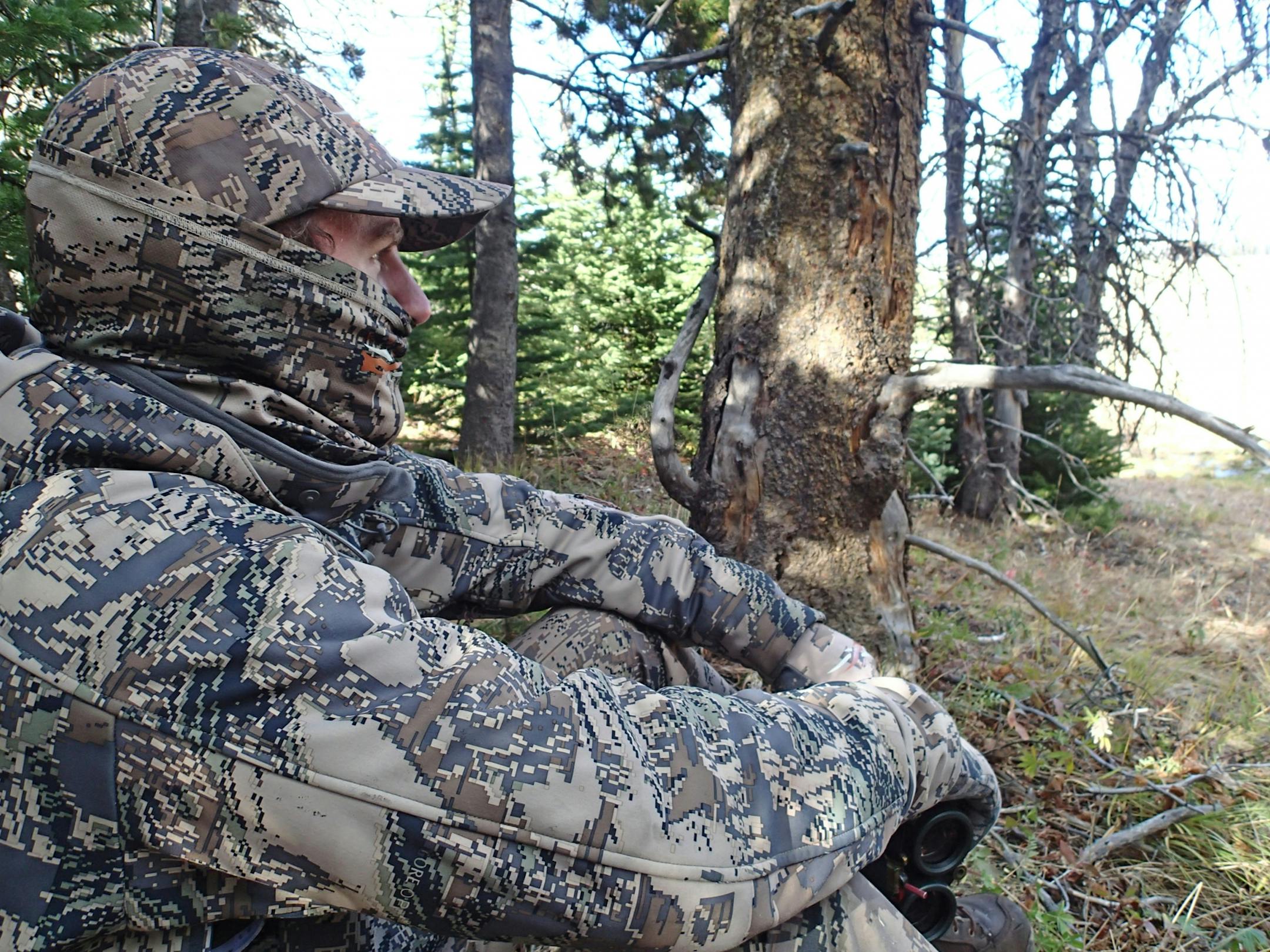 Clad in lightweight, breathable camouflage clothing for hunting elk on foot in the Montana mountains, Trevor Anderson watches a distant hillside, from which a bull elk has bugled.