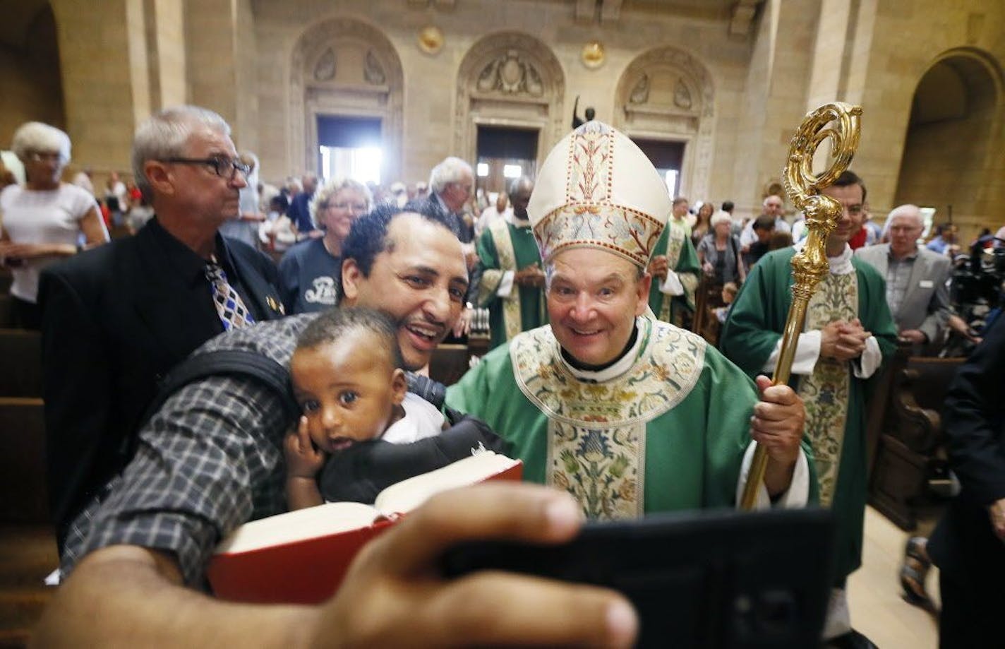 Aime held his son Raphael as they took a selfie with Archbishop Bernard Hebda who greeted parishioners after celebrating his first mass at the St. Paul Cathedral Sunday July 12, 2015 in St. Paul MN.